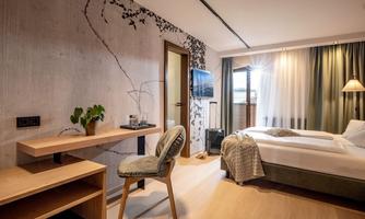 A modern hotel room with a comfortable bed and a desk.  
Large windows provide plenty of daylight and offer a view outside.