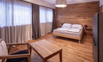 A bright bedroom with wooden paneling and large windows. The room is furnished with a bed, a table, and a chair.