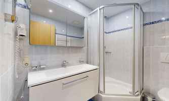 A modern bathroom with a shower and a sink. The walls are in light colors and there are large mirrors.