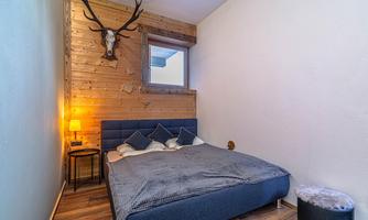 A cozy bedroom with a large bed and wooden paneling. A deer antler hangs on the wall, and there is a small table with a lamp.