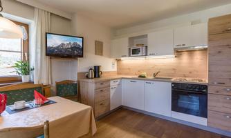 A modern kitchen with wooden details and a television. The room is bright and friendly, with a table and chairs.