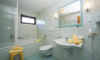 A modern bathroom with tiles in light colors. It is equipped with a bathtub, a sink, and a window for daylight.