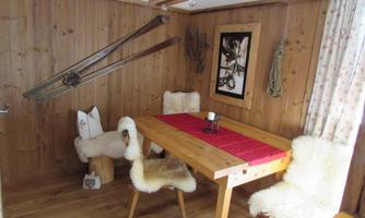 A cozy dining area with a wooden table and chairs with sheep skins. Skis are hanging on the wall and there is a decorative photograph.