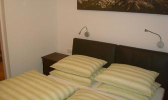 A cozy bedroom with a double bed and striped pillows. A landscape picture hangs on the wall, and there are bedside lamps.