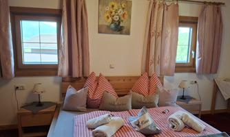 A cozy bedroom with a large bed and pink checkered pillows. The walls are painted light and decorated with curtains in matching colors.