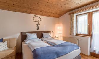 A cozy bedroom with two beds and a wooden ceiling. A small couch and a window with curtains complete the room.