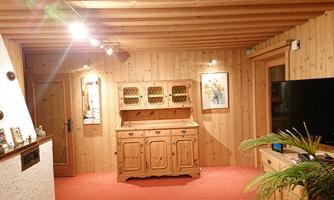 A cozy room with wooden paneling and a red carpet. In the foreground, there is a wooden cabinet and a television on the wall.