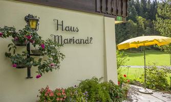 A charming house with the inscription "Haus Mariandl".  
In front of the building are colorful flowers and a yellow sun umbrella.