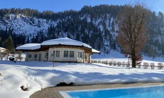 A modern house in the snow with a swimming pool and a wintry landscape. The surroundings are surrounded by mountains and trees.
