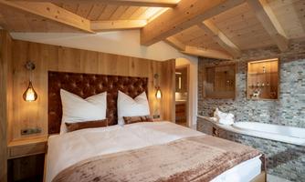 A cozy bedroom with a wooden bed and soft pillows. The room features an elegant bathtub and warm, inviting light.