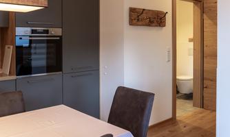 A modern dining room with a table and chairs. In the background, a door to a bathroom is visible.