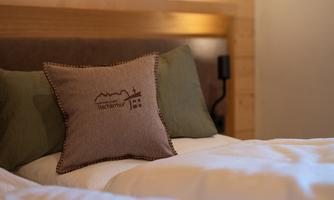 A comfortable bed with a decorative pillow and green pillow covers. In the background, wood paneling is visible.