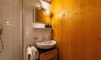 A modern bathroom with a round wash basin on a wooden cabinet. The walls are partially tiled and paneled with wood.