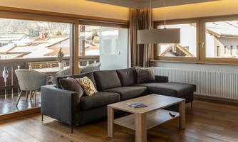 A modern living room setup with a comfortable sofa and an elegant coffee table. Large windows offer a view of the surrounding houses.