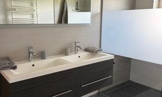 A modern bathroom with a double sink and large mirrors. The walls are bright and the floor has a dark tile look.