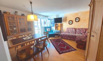 A cozy living area with a dining table and chairs. Decorative pillows are on the couch and the room is bright and inviting.