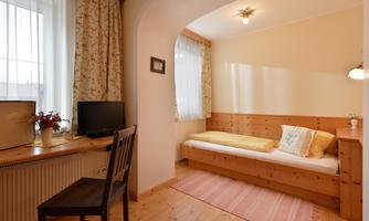 A cozy room with a bed and a desk. It has bright walls and a window with curtains.