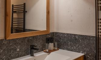 A modern bathroom with a wooden vanity and a large mirror. The walls are adorned with gray stone and a towel radiator.