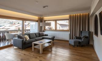 A modern living room with a large window and beautiful views. The furniture is simple and comfortable, the room has a bright wooden floor.