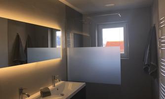 A modern bathroom with a large mirror and elegant sinks. The light is soft and the window offers a view outside.