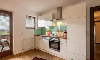 A modern kitchen with white cabinets and a green wall. There is a refrigerator, an oven, and plenty of sunlight through the window.