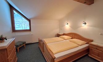 A cozy bedroom with a double bed and wooden furniture. A large window provides plenty of daylight.