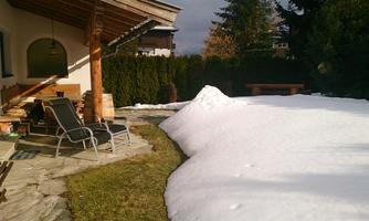 A terrace with loungers and a snow-covered plot. In the background, tall trees and a beautiful sky can be seen.