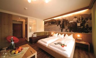 A cozy hotel room with a double bed and a wooden ceiling. On the wall is a large picture of horses and farmers.