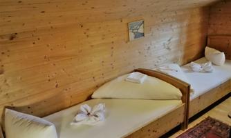 A cozy room with two wooden beds and cushions. The walls are made of wood and there is a small picture on the wall.
