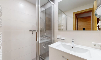 A modern bathroom with a shower and a sink. The walls are in light colors, and there are large mirrors.
