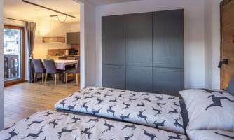 A cozy bedroom with two beds and a modern décor. In the background, a dining area is visible.