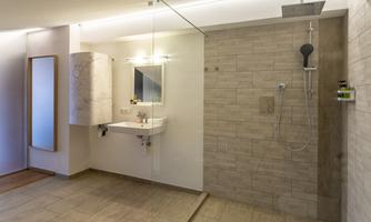 A modern bathroom with a walk-in shower and a large mirror. The walls are tiled in light shades, conveying an elegant impression.