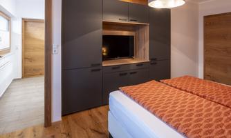 A modern bedroom with a comfortable bed and a flat-screen TV in a cabinet. The walls are in soft wood tones, and the room feels inviting and cozy.