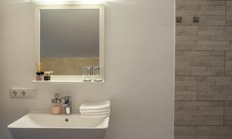 A modern bathroom with a simple sink and a mirror. The walls are light and decorated with tiles.