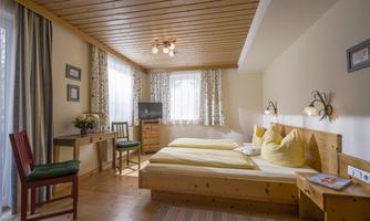 A cozy bedroom with two beds and yellow pillows. Large windows let in plenty of light and there is a small table with chairs.
