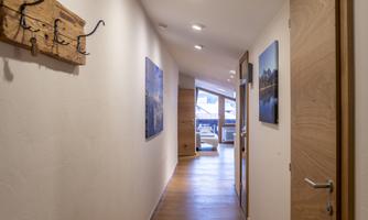 A bright hallway with wooden flooring and walls in neutral colors. Pictures hang on the wall and a wooden luggage rack is present.
