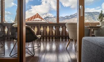 A cozy terrace with seating and a view of the mountains. The sky is blue and the atmosphere is inviting.