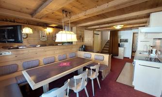 A cozy kitchen with wooden ceilings and a large dining table. The room is well-lit and has an inviting atmosphere.