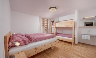 A bright bedroom with two beds and a bunk bed. The room has a modern, minimalist style and wooden accents.