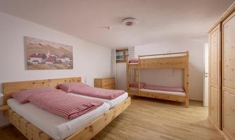 A cozy room with a double bed and a bunk bed. The walls are light and there are wooden shelves as well as a wall mural.