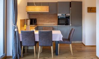 A modern kitchen with a dining area. The table is set and there are cozy chairs as well as gray kitchen cabinets.
