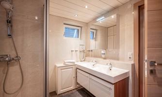 A modern bathroom with a shower, two sinks, and bright walls. There are large mirrors and plenty of daylight from the windows.