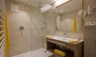 A modern bathroom with a glass shower and a wooden vanity. Yellow towels and a large mirror create an inviting look.