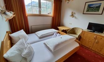 A cozy bedroom with two single beds and wooden furniture. Large windows provide a view of the mountains and allow for plenty of light.