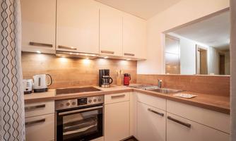 A modern kitchen with bright furniture and wooden accents. The equipment includes a stove, a coffee machine, and a sink.