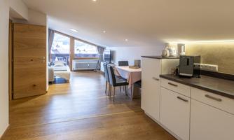 A modern apartment with wooden flooring and an open kitchenette. Large windows provide plenty of natural light and a view of the living area.