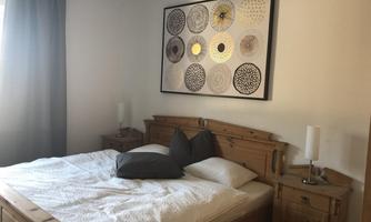 A cozy bedroom with a large bed and decorative wall art. There are wooden furniture and soft light coming through the window.