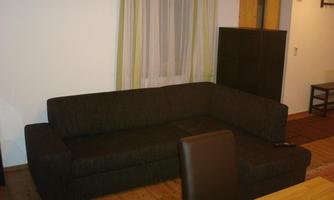 A modern, dark brown sofa in a living space. In the background, curtains and a wooden floor are visible.