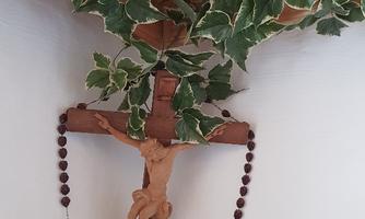 A wooden cross with a depiction of Jesus Christ hangs on the wall. Above it, green plants are climbing.