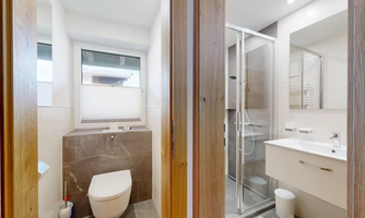 A modern bathroom with a shower and sink. The walls are brightly tiled, and there are large windows for natural light.